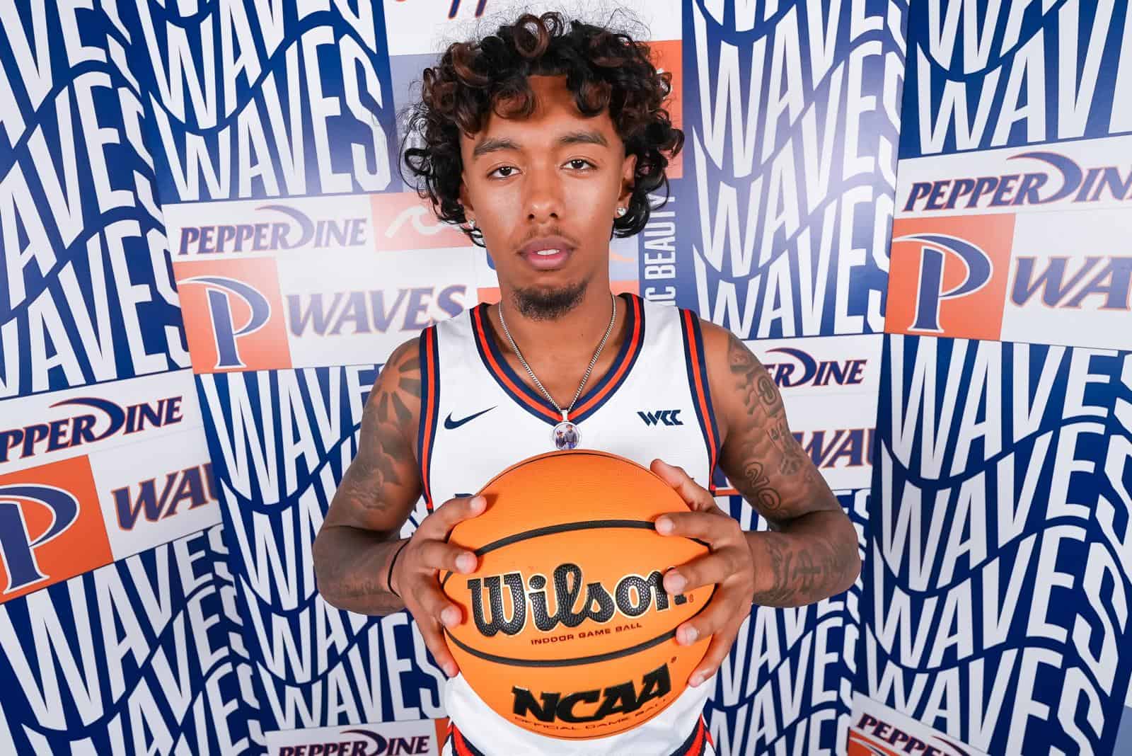 A young basketball player holding an orange Wilson NCAA basketball in front of a branded blue and white Wave Waves backdrop.